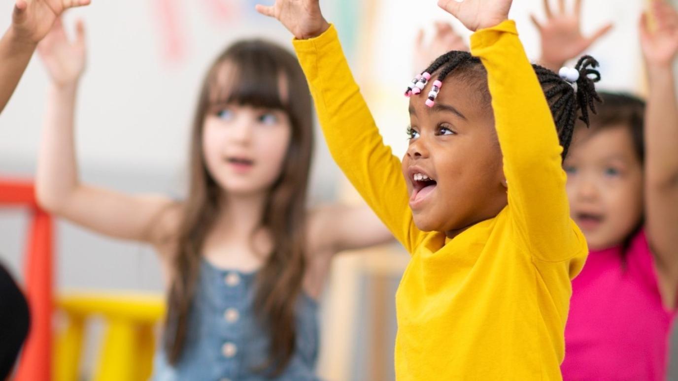 Excited children in a early years learning centre joyously throwing their hands