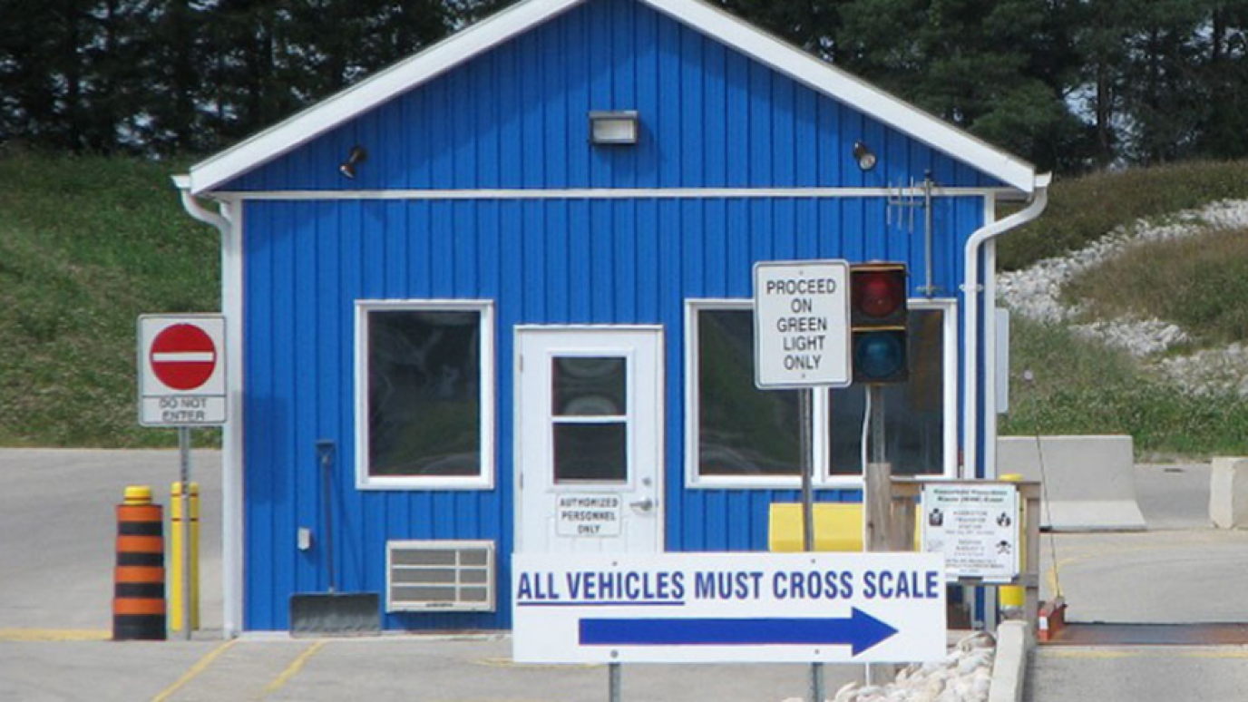 Small blue scalehouse at a waste facility with traffic signs direction vehicles onto the scales