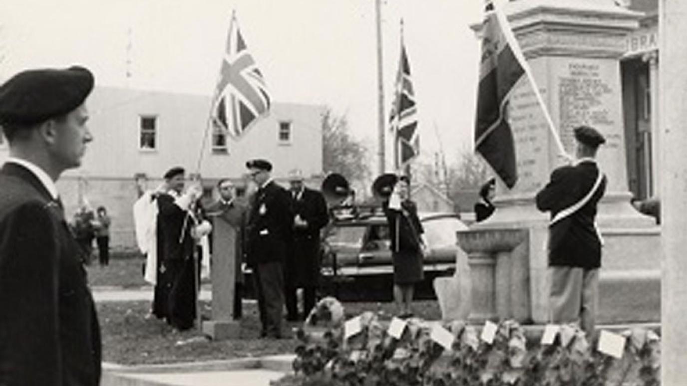 Historic black and white photo of people gathered by a cenotaph for a remembrance ceremony