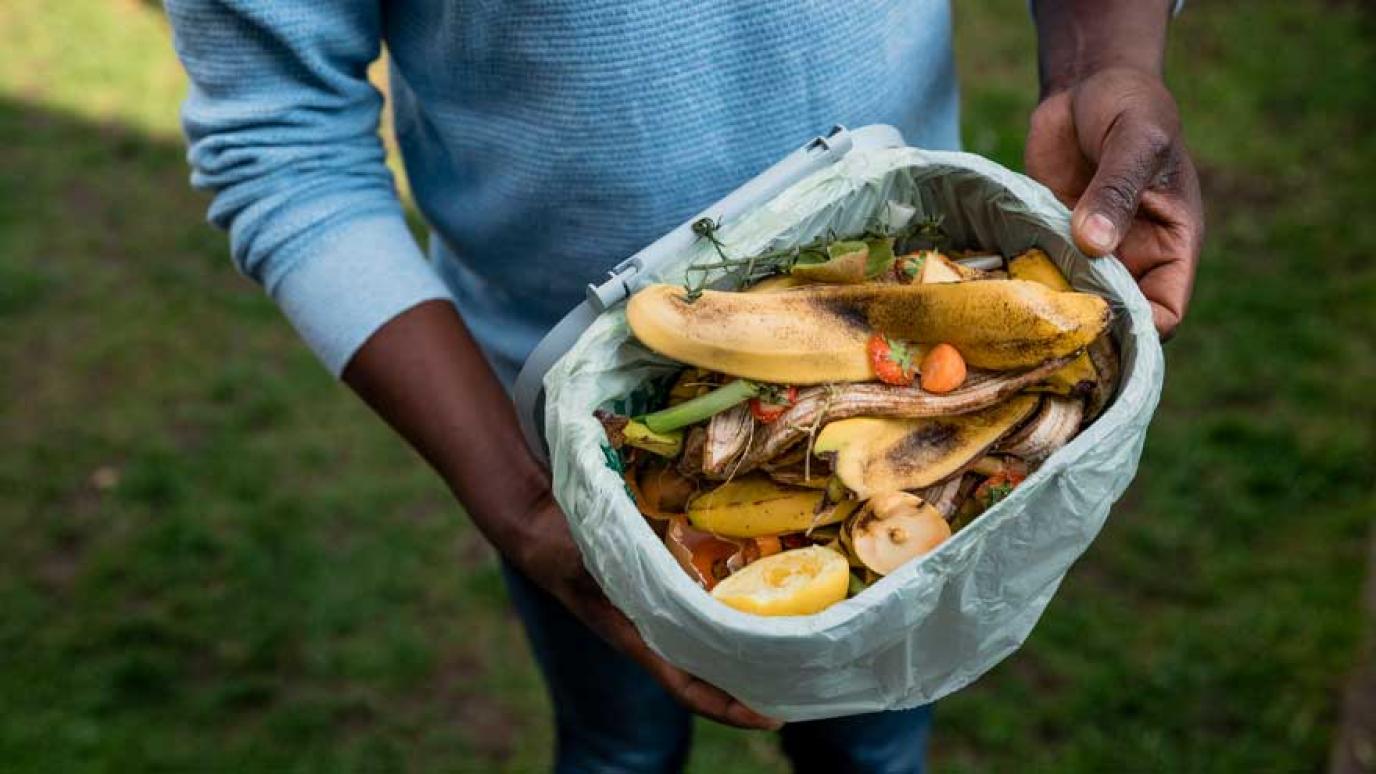 An unrecognizable person holding their BPI lined plastic composting bin 