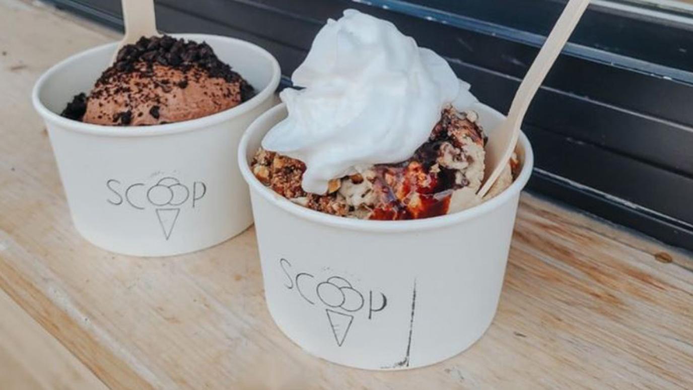 Two cups of ice cream with the Scoop logo on the front; one full of chocolate ice cream with cookie crumbs on top, the other filled with a vanilla and whipped cream toppings. 