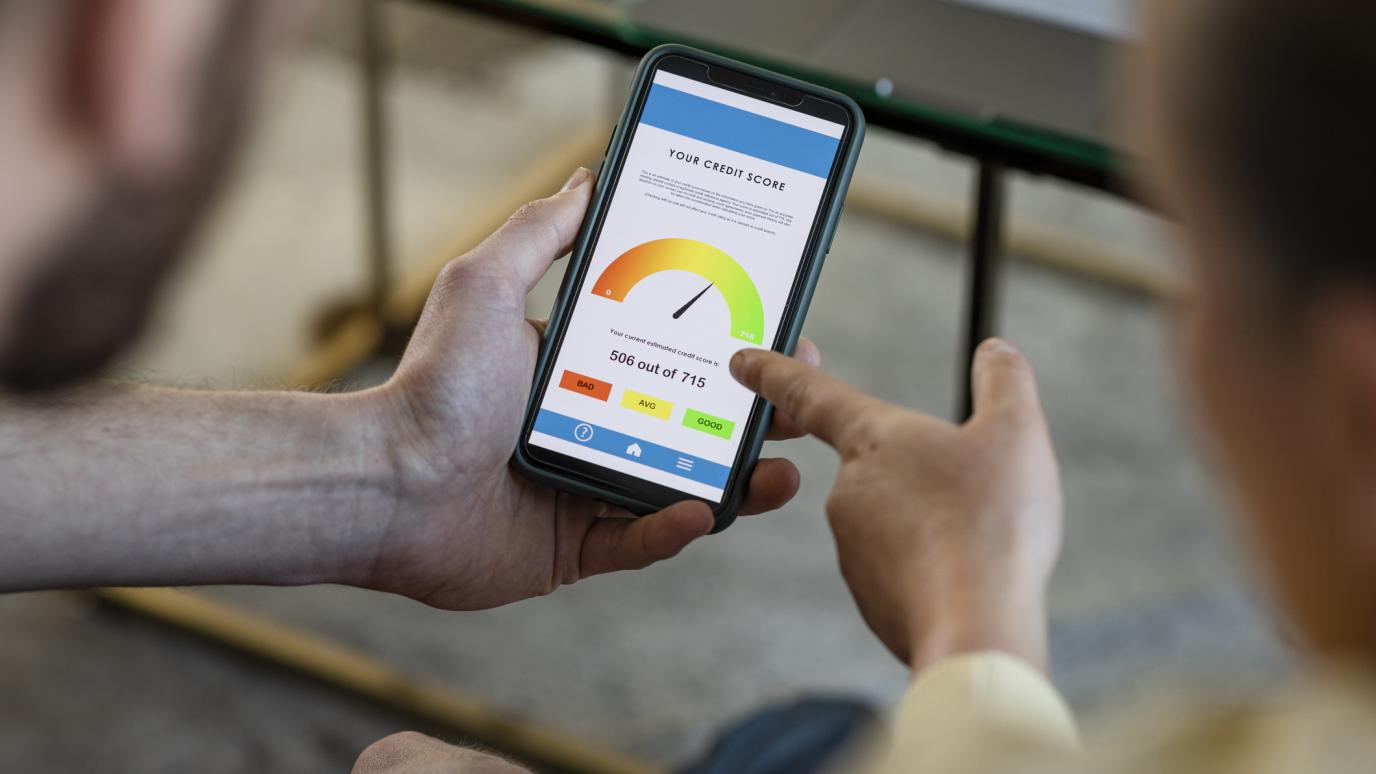 A close up of a man holding a phone with a credit score metre on the screen. A woman