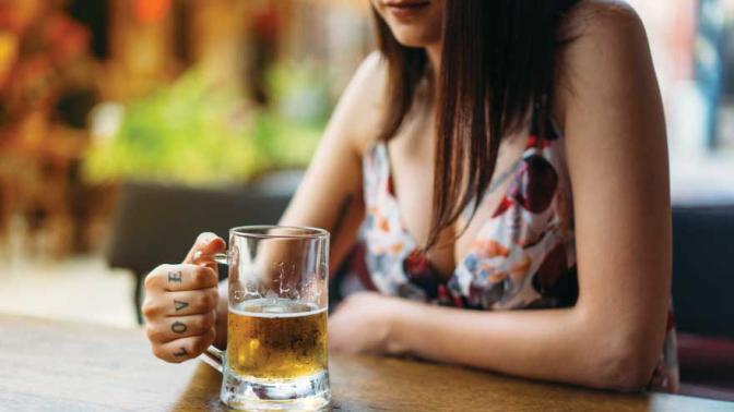 Beautiful woman with tattoos on her fingers sitting at a bar holding a pint glass of beer