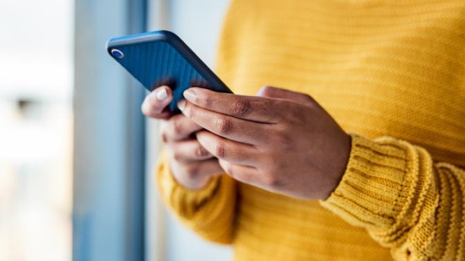Unrecognizable woman in yellow sweater using a mobile phone indoors