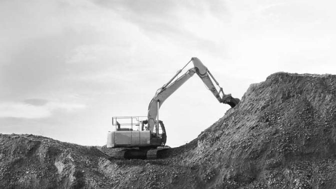 Excavator bulldozer in sandpit with raised bucket over cloudscape sky.