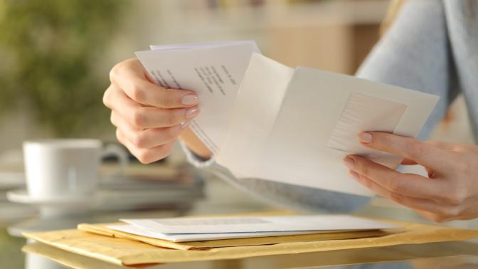 Close up of girl hands opening an envelope with a letter inside on a desk at home.