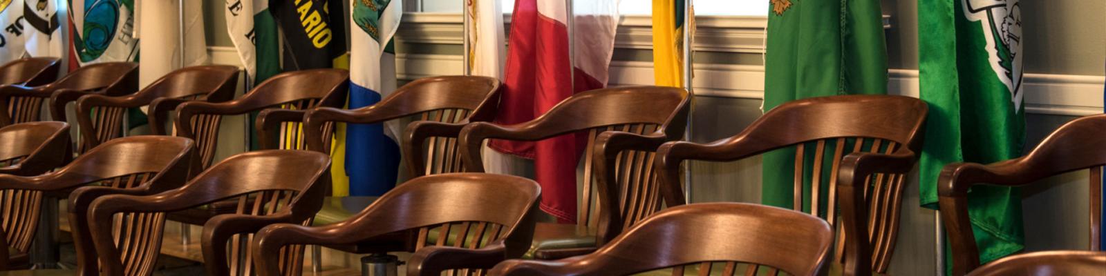 Gallery of chairs in Council Chambers with rows of flags in the background