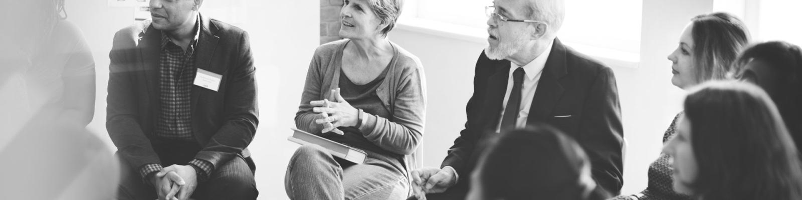 Black and white shot of a group of people gathered in a circle to listen to a speaker