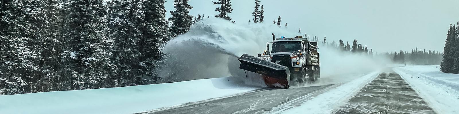 Snowplow plowing snow off a two lane rural tree lined highway