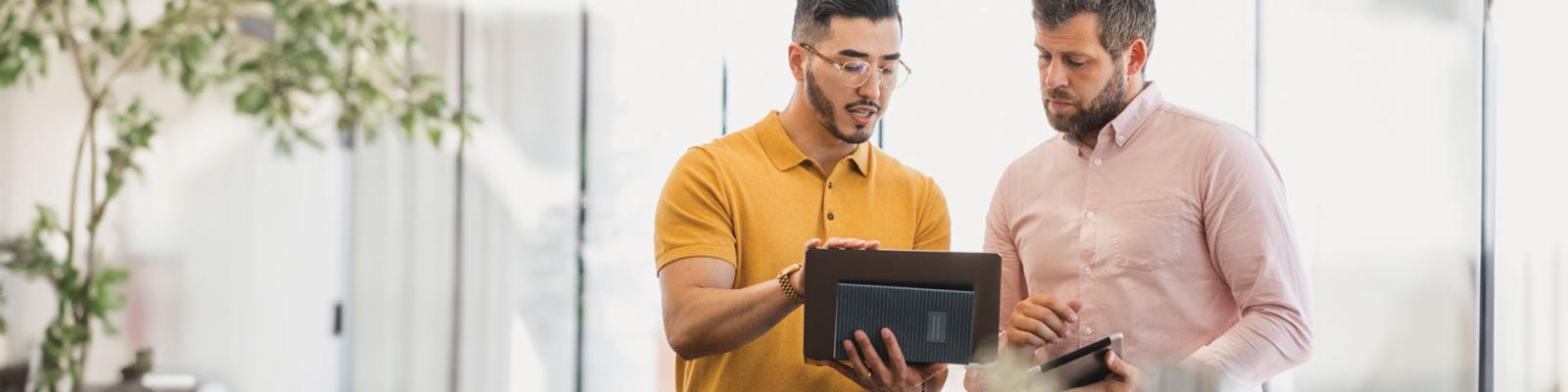 Two smart casually dress men reviewing plans on an ipad in an office setting