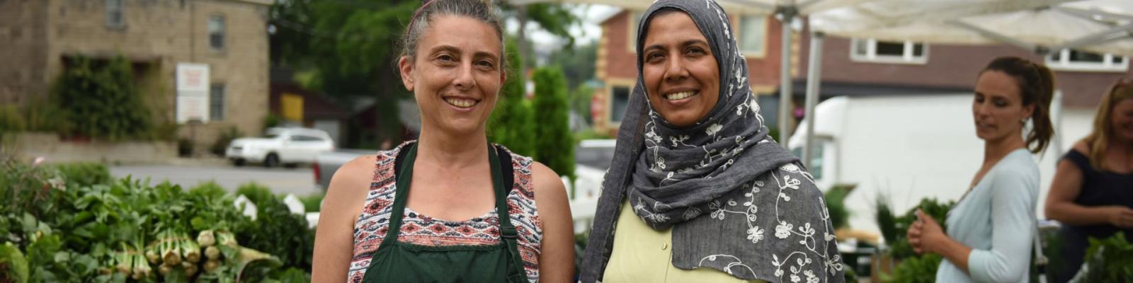 Two smiling female farmers selling products at a farmers market