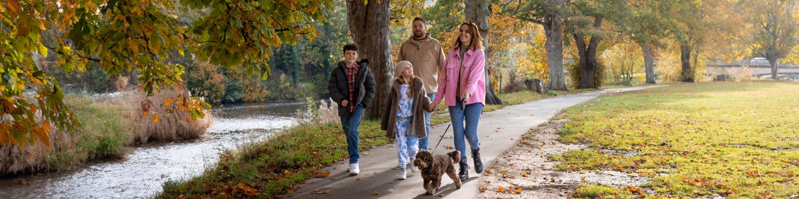 A family with two children and a dog, walking together in a park along a footpath.