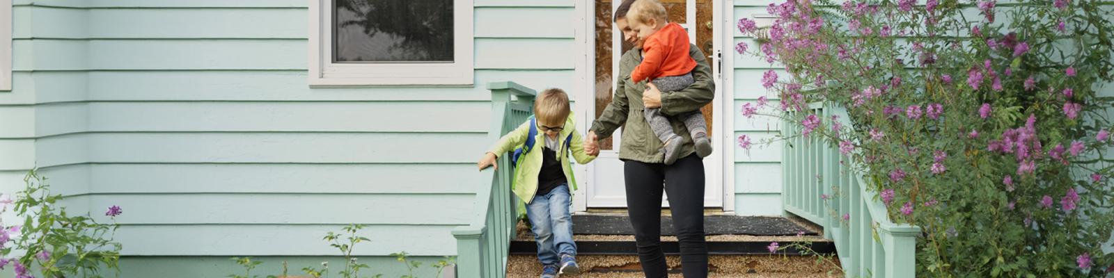 Mother holding a child in her arms while helping another child down the front steps of their home