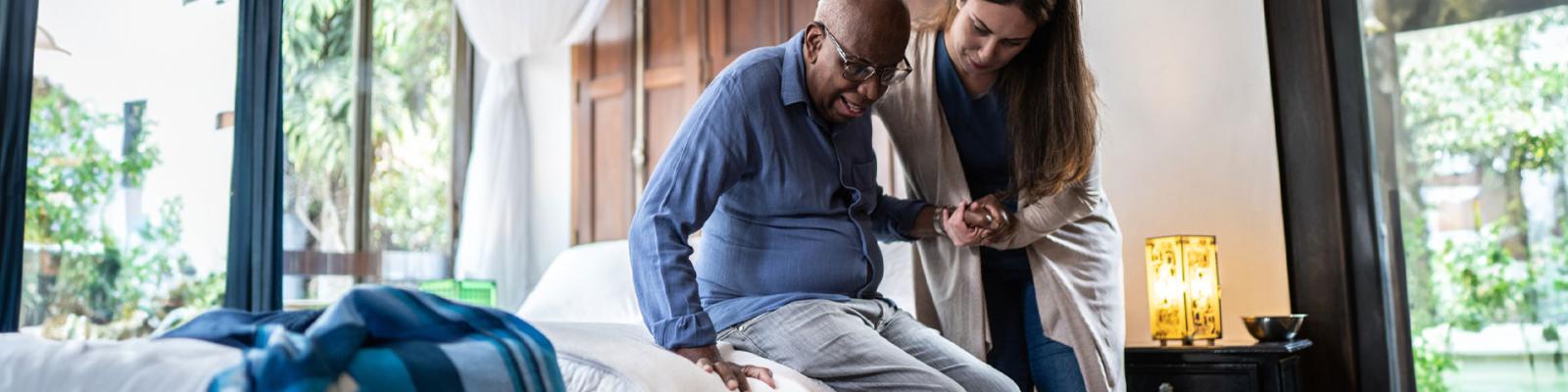 Caregiver helping a senior man standing up at a home