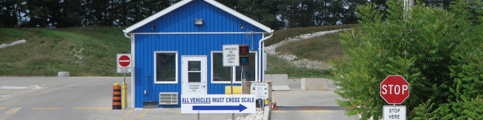 Small blue scalehouse at a waste facility with traffic signs direction vehicles onto the scales