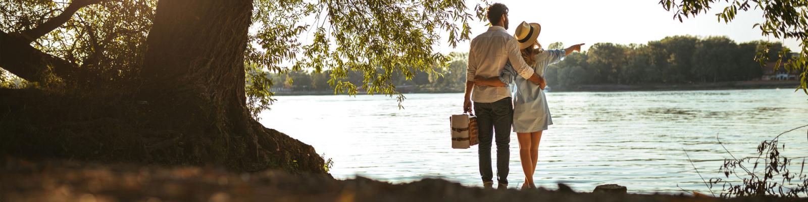 Couple standing by a lake with a picnic basket enjoying the summers day