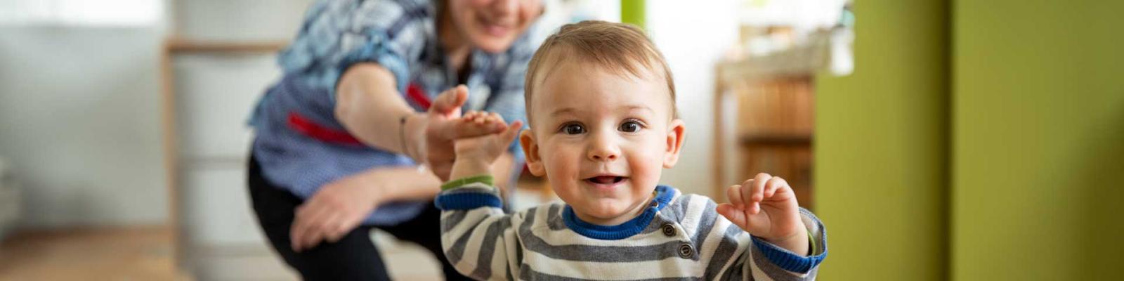Childcare worker supporting a toddler with his first attempts to walk