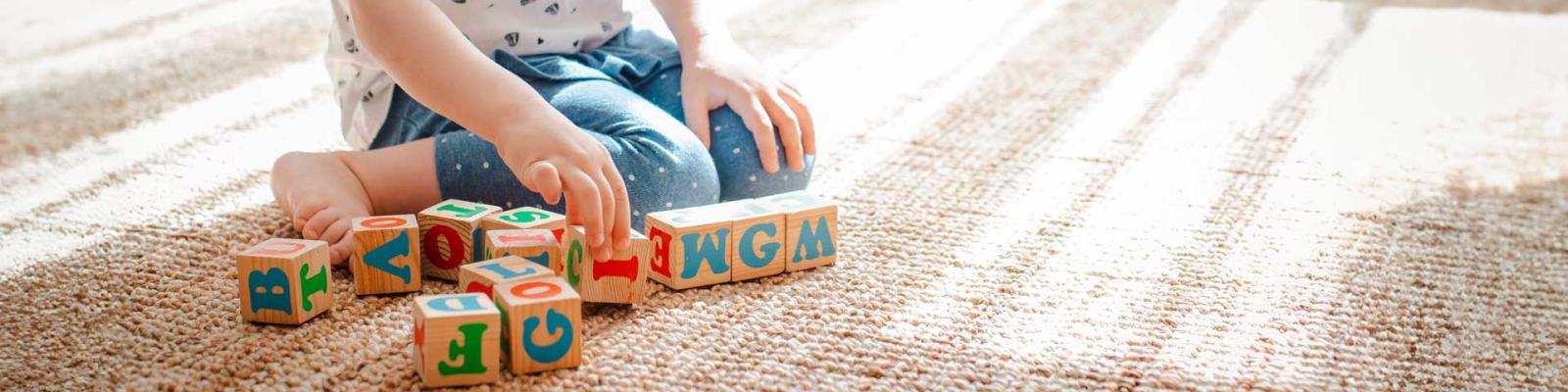 Cropped view of child playing with wooden cubes with colorful letters on a sunlit carpet