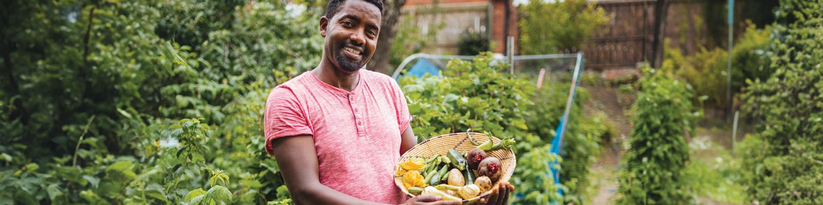 Man looking at the camera holding a wicker basket with home grown vegetables inside.