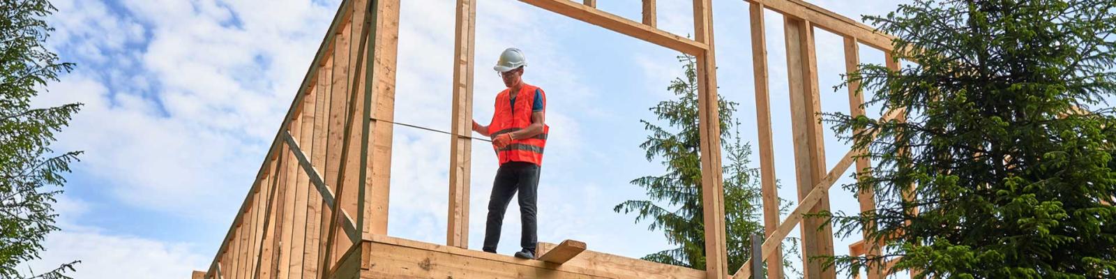 Carpenter measures distance with tape measure while building wooden frame house