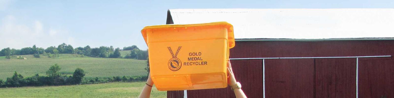 Person holding up the Gold recycling box against a rural background