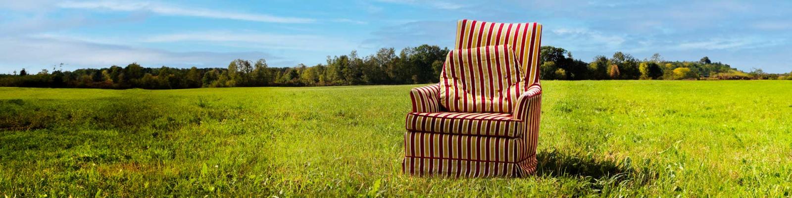 Old striped arm chair sits in a grassy field beneath a blue sky