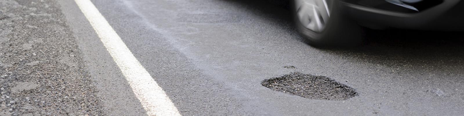 A pothole on a road with a card driving past