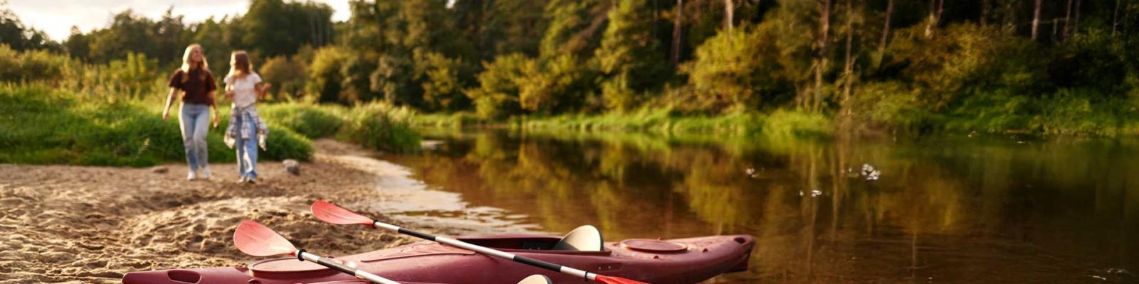 Two women walking towards a red kayak 
