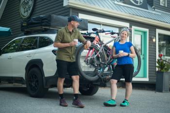 two people outside cafe holding coffee leaning against truck with bikes on the back