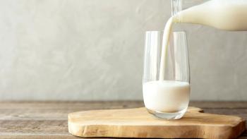 Fresh milk poured into a glass cup from a bottle. The glass stands on a wooden stand on a rustic wooden table.