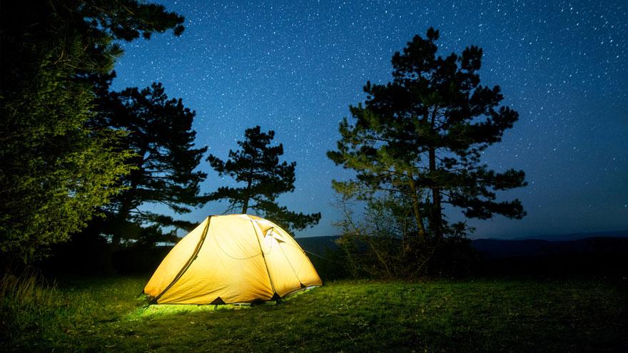 Glowing camping tent in the night forest under a starry sky