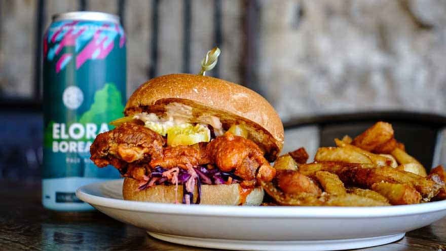 Fried chicken sandwich on a plate with fries next to a can of Elora Borealis