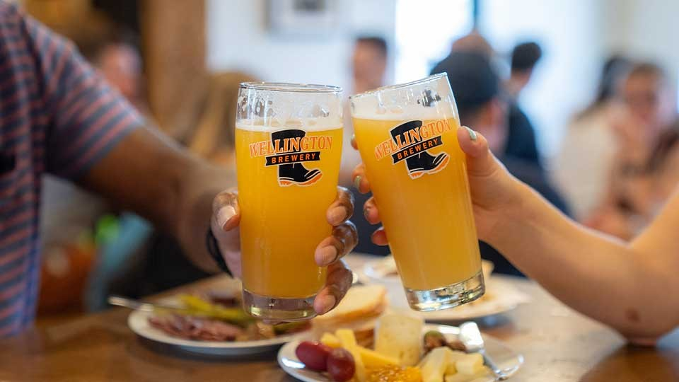 Two individuals making a celebratory toast with Wellington Brewery beer.