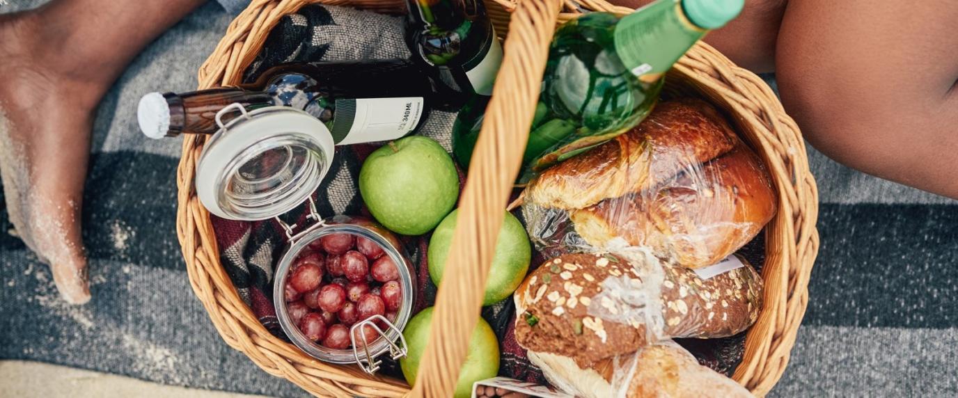 gift basket full of fruit, bread and beverages on a blanket.