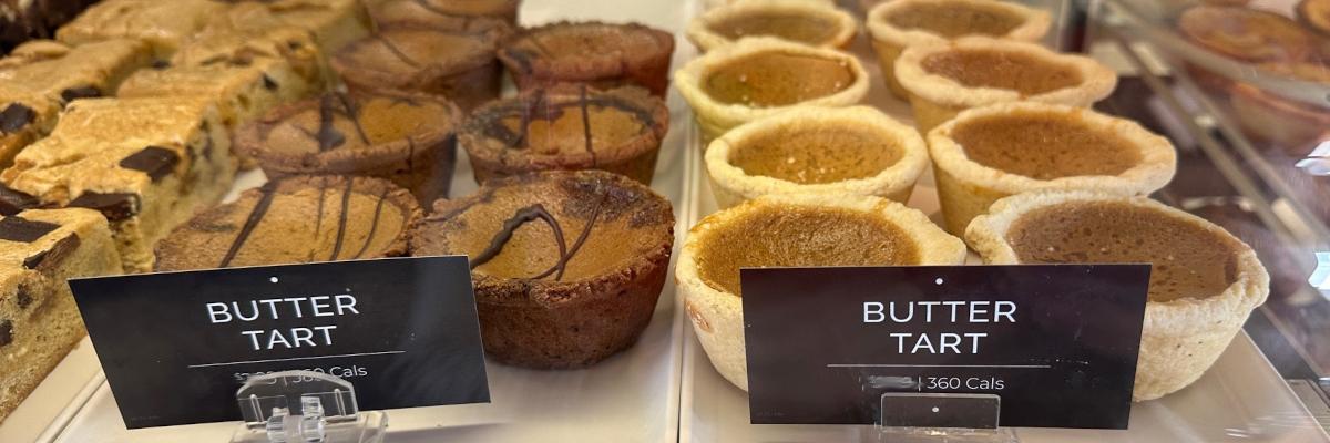 Butter tarts displayed in a bakery case, with labels identifying different varieties.