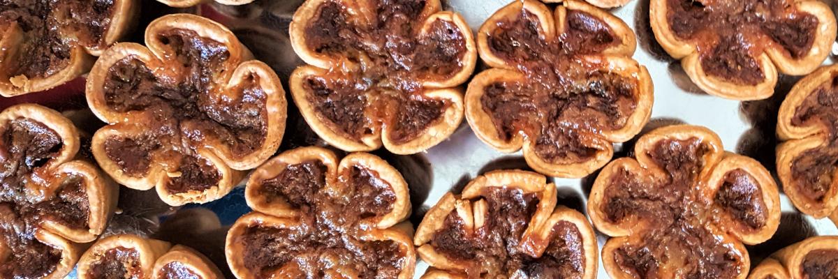 Close-up of multiple flower-shaped butter tarts with rich, caramelized filling.